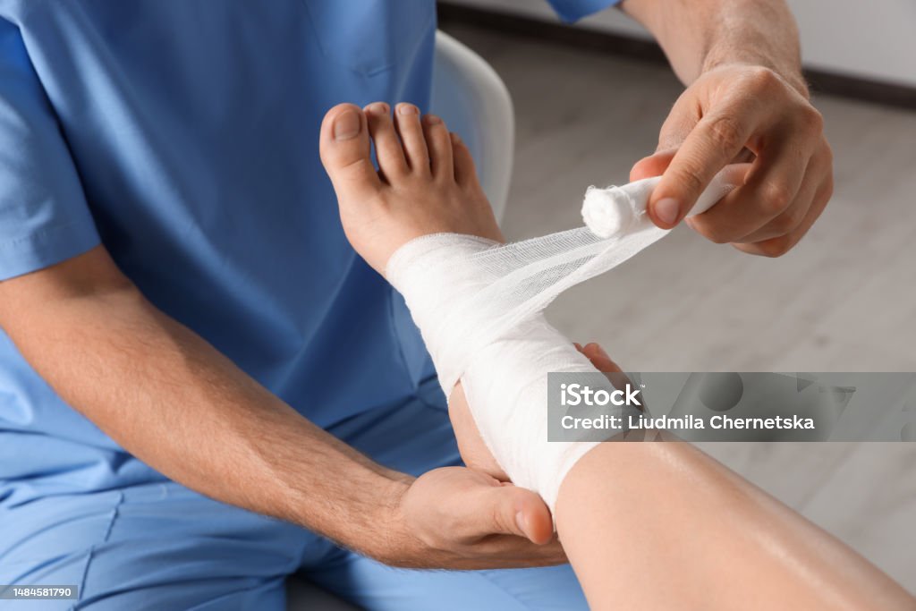 Doctor applying bandage onto patient's foot in hospital, closeup